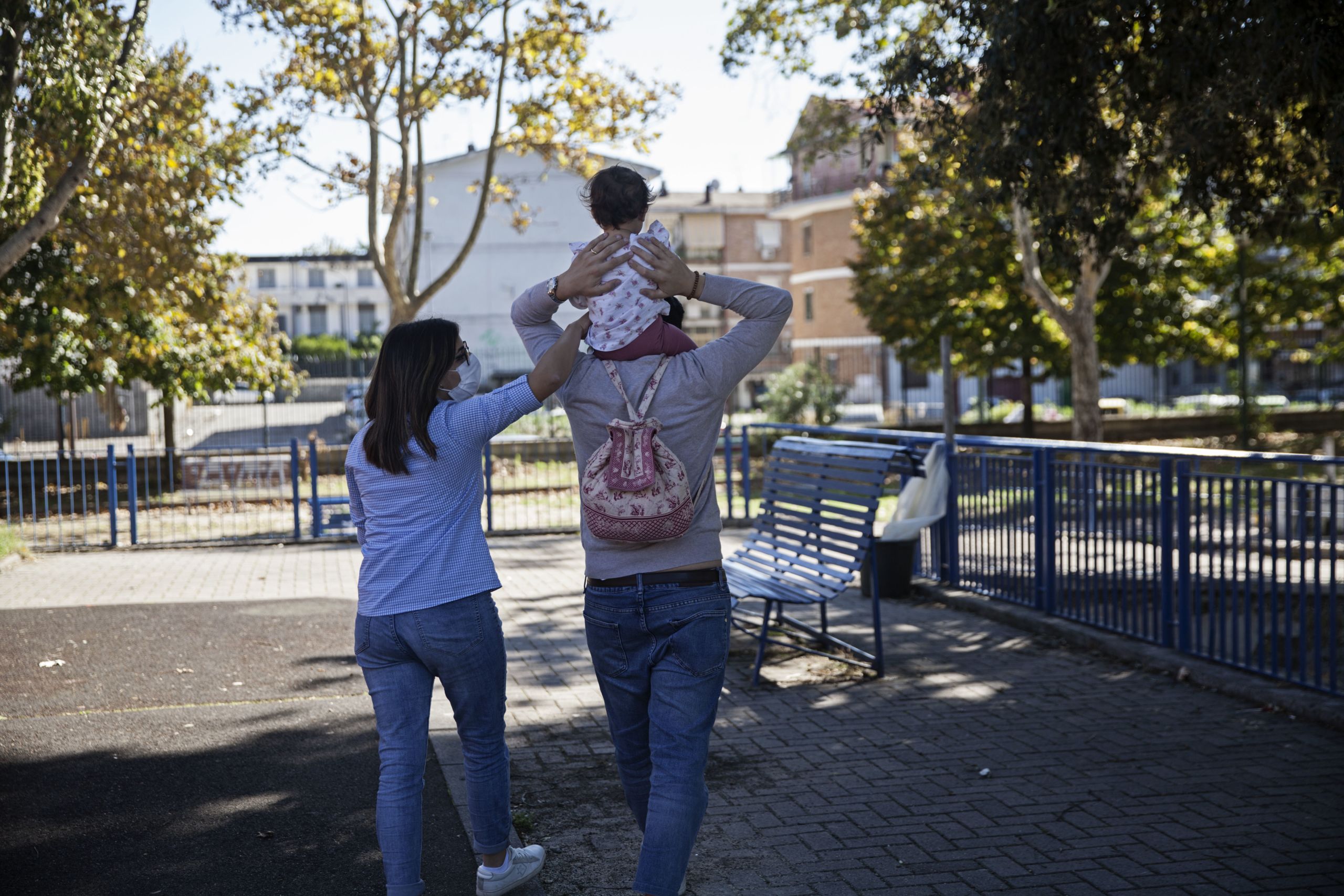 Una mamma e un papà di spalle con una bambina in braccio passeggiano in un cortile